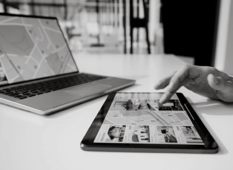 Digital property listings and maps displayed on a tablet and laptop during a leasing discussion.